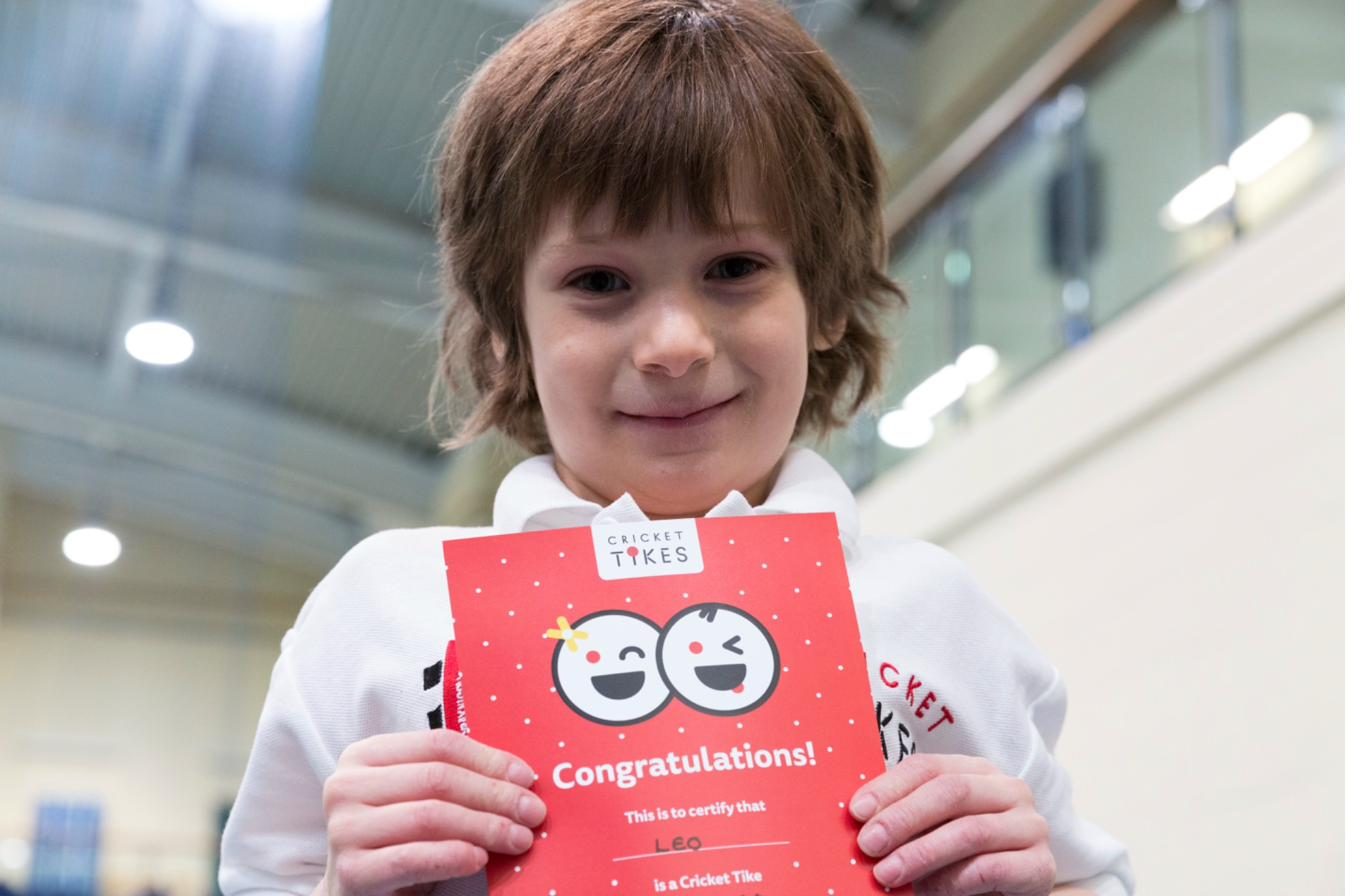 Child proudly holding a Cricket Tikes certificate